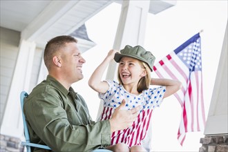 Caucasian daughter wearing hat of soldier father