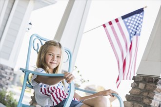 Caucasian girl sitting on porch near American flag