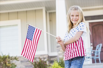 Smiling Caucasian girl waving American flag near house