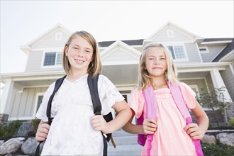 Caucasian sisters with backpacks smiling near house