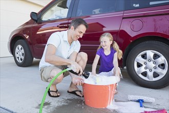 Caucasian father and daughter washing car in driveway