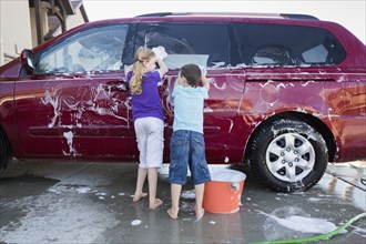 Caucasian children washing car in driveway