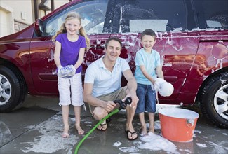 Caucasian father and children washing car in driveway