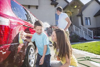 Caucasian family washing car in driveway