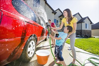 Caucasian family spraying water on car in driveway