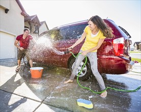 Caucasian couple playing while washing car in driveway