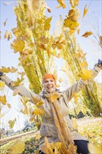 Older Caucasian woman playing in autumn leaves