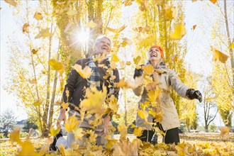 Older Caucasian couple playing in autumn leaves
