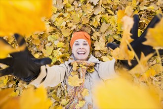 Older Caucasian woman playing in autumn leaves