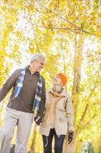 Older Caucasian couple walking under autumn trees