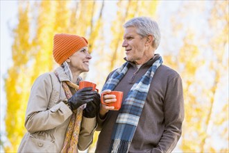 Older Caucasian couple drinking coffee near autumn trees
