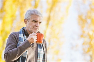Older Caucasian man drinking coffee near autumn trees