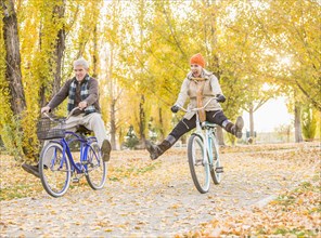 Older Caucasian couple riding bicycles on autumn leaves