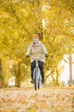 Older Caucasian woman riding bicycle on autumn leaves