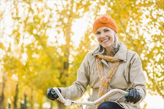 Older Caucasian woman riding bicycle under autumn trees