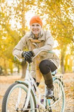 Older Caucasian woman riding bicycle on autumn leaves