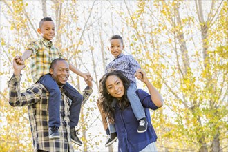 Parents carrying children on shoulders near autumn trees