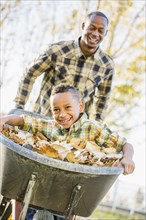 Father pushing son in wheelbarrow in autumn leaves