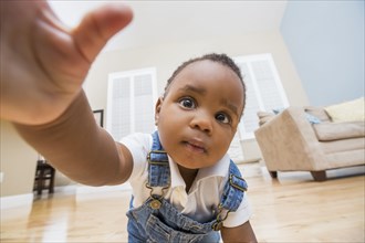Black baby reaching for camera on living room floor