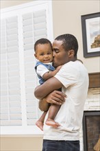 Black father kissing baby son in living room