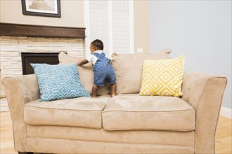 Black baby climbing on sofa in living room