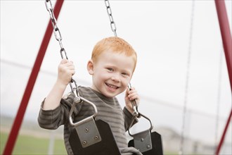 Caucasian boy sitting on playground swing