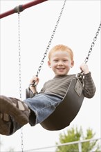 Caucasian boy sitting on playground swing