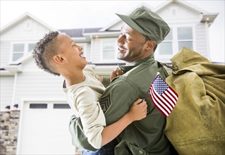 Returning soldier hugging patriotic son outside house