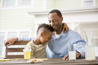 Black father and son hugging at table in backyard