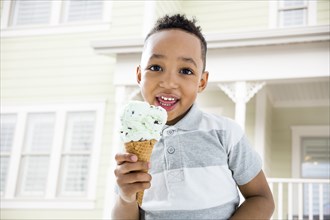 Mixed race boy eating ice cream cone in backyard