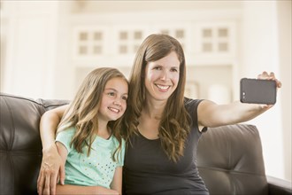 Caucasian mother and daughter taking selfie with cell phone on sofa