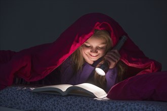 Caucasian girl reading under blanket at night