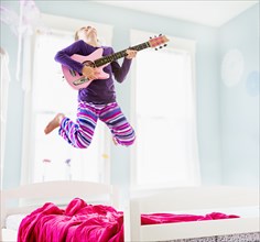 Caucasian girl playing guitar on bed