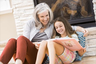 Caucasian grandmother and granddaughter reading book by fireplace