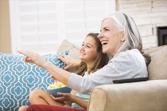Caucasian grandmother and granddaughter watching television on sofa