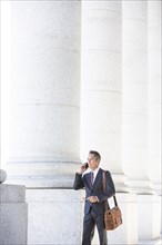 Mixed race businessman talking on cell phone under columns