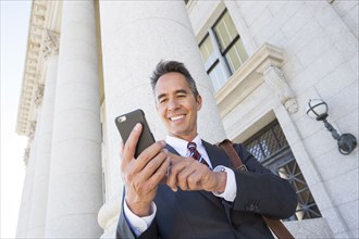 Mixed race businessman using cell phone outside courthouse