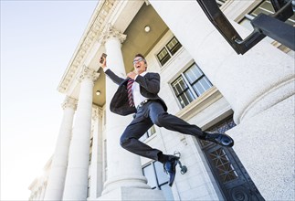 Mixed race businessman jumping for joy outside courthouse
