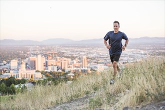Mixed race man running on hilltop over Salt Lake City