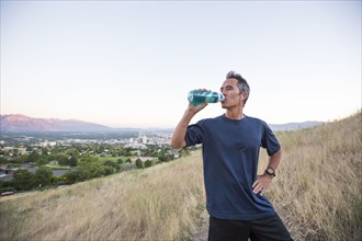 Mixed race man drinking water bottle on hilltop