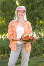 Caucasian woman holding basket of vegetables in garden