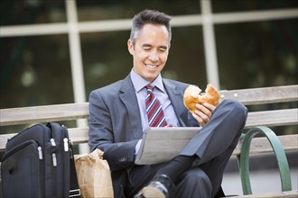 Mixed race businessman eating and using digital tablet