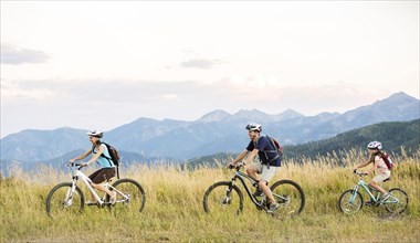 Caucasian family riding mountain bikes in field