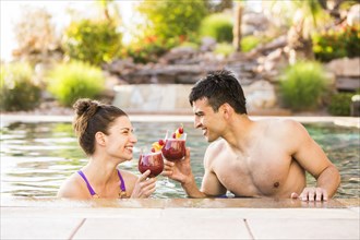 Couple toasting with cocktails in swimming pool