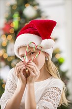 Caucasian girl peering through Christmas candy canes