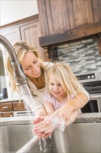 Caucasian mother and daughter washing hands in kitchen sink