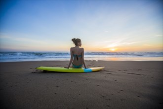 Caucasian woman sitting on surfboard on beach