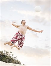 Caucasian man hitting volleyball on beach