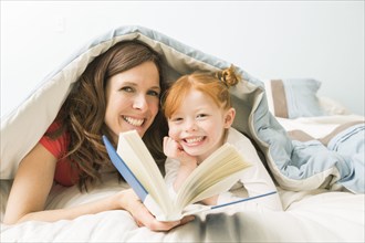 Caucasian mother and daughter reading book in bed
