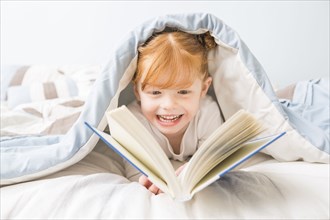 Caucasian girl reading book in bed